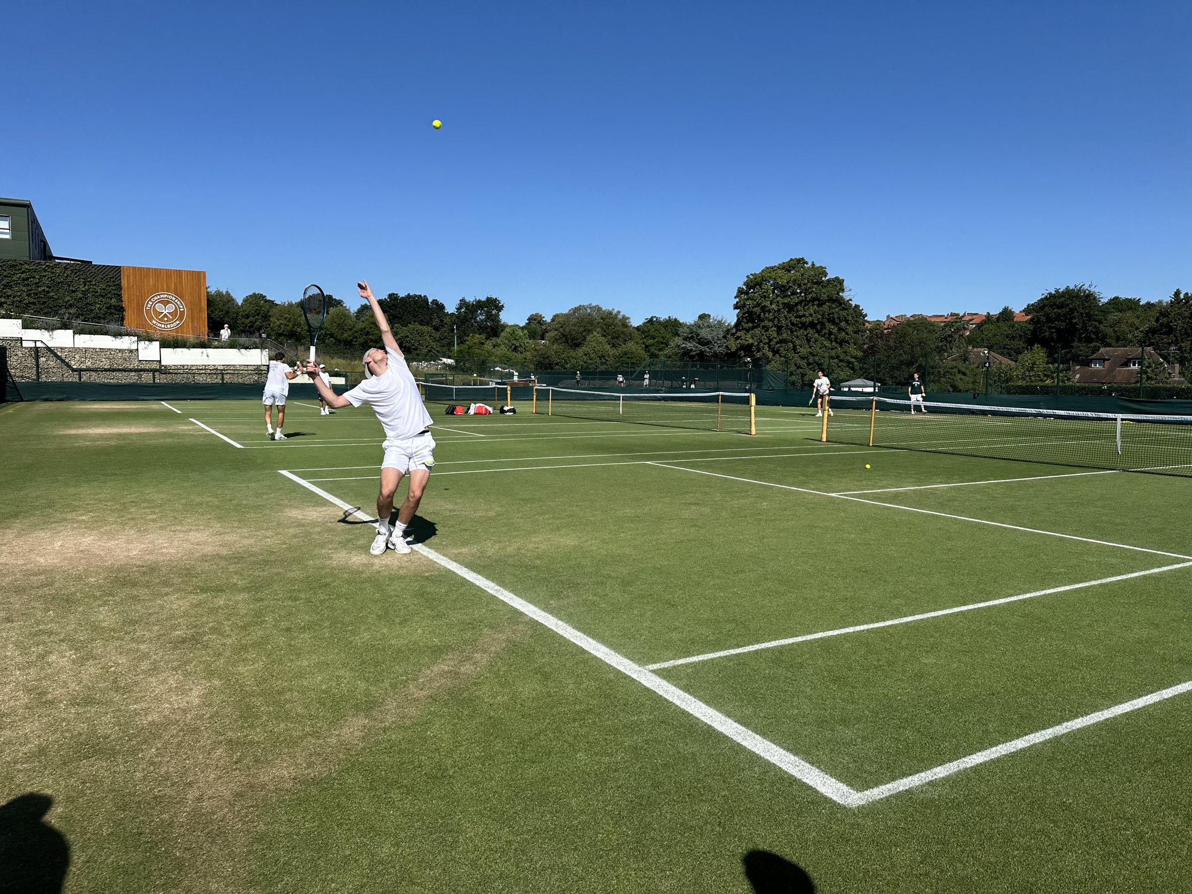 A player serving on a grass practice court at Wimbledon